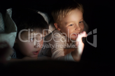 Two boys watching movie or cartoon on pad at night