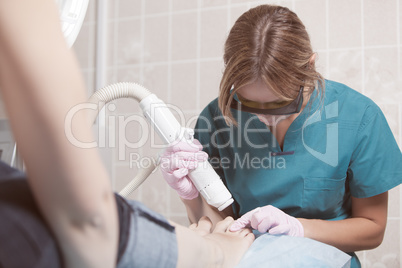 Female cosmetician doing foot therapy using laser