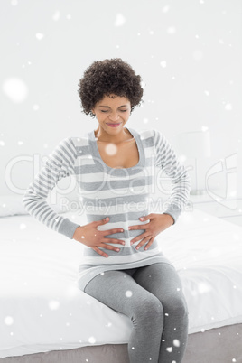 Composite image of casual woman with stomach pain sitting in bed