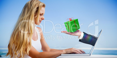 Composite image of pretty blonde using her laptop at the beach