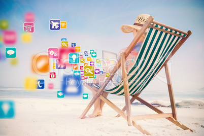 Composite image of woman in sunhat sitting on beach in deck chai