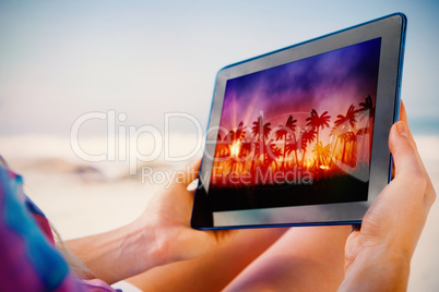 Composite image of woman sitting on beach in deck chair using ta