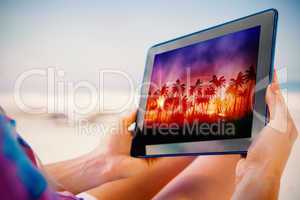 Composite image of woman sitting on beach in deck chair using ta