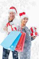 Composite image of festive mature couple in winter clothes holdi