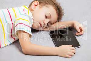Tired sleeping child boy holding tablet computer