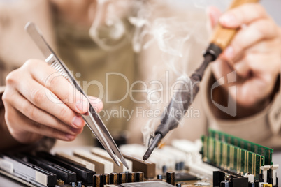 Human hand holding soldering iron repairing computer circuit boa