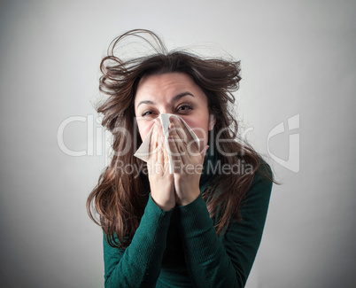 Young woman blowing her nose with paper tissue.