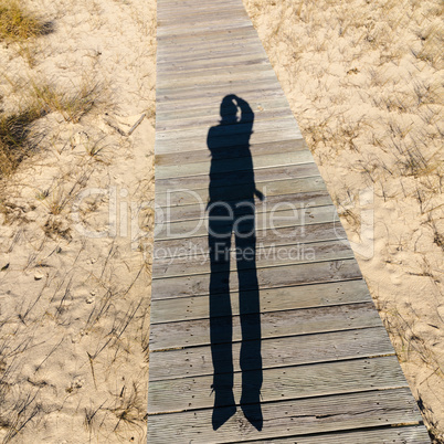 Elongated Shadow Jumping Man on a Wooden Walkway