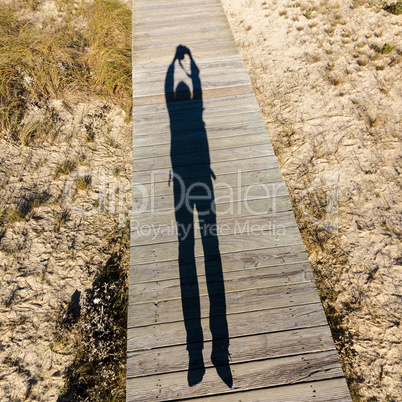 Elongated Shadow Jumping Man on a Wooden Walkway