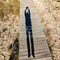 Elongated Shadow Jumping Man on a Wooden Walkway