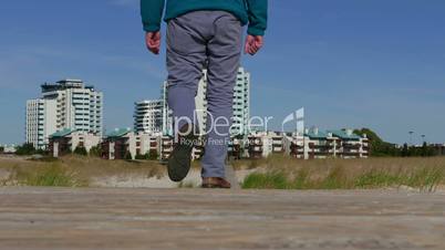 A Man Walks by a Wooden Walkway to Town, view from the back