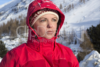 Woman with red jacket looks into the distance in the mountains