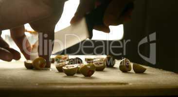 Hand slicing olives on a chopping board