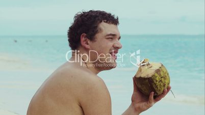 Man on the beach drinking from coconut