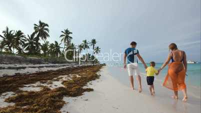 Family of three walking along the beach in tropics