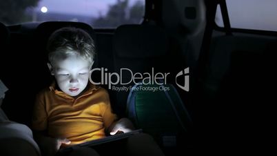 Little boy using tablet pc during car travel at night