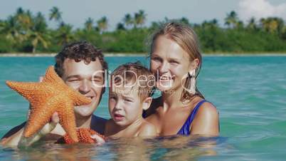 Parents and son in sea water holding starfish