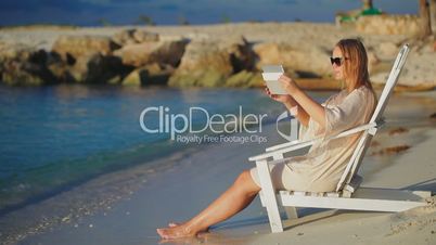 Woman with pad making photos of sea sitting in deck chair on beach