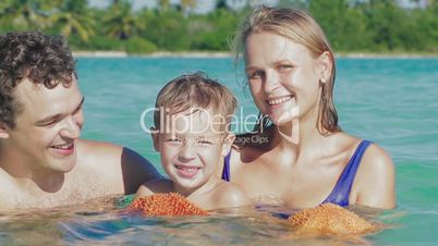 Parents and their little son in sea water holding starfish