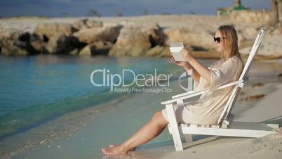 Woman with pad making photos of sea sitting in the deck chair on beach