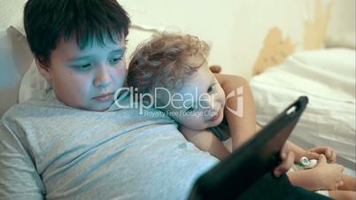 Two brothers with pad lying in bed. Entertainment tablet PC