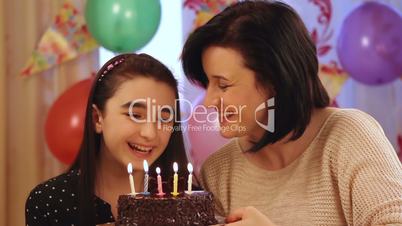 Happy mother and daughter blowing candles of birthday cake
