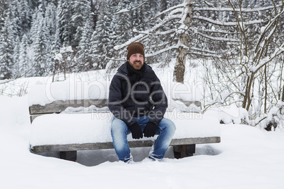 Young man is sitting on a snowy park bench