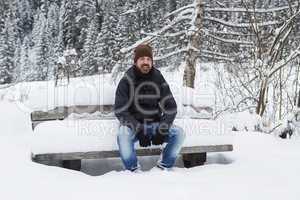 Young man is sitting on a snowy park bench