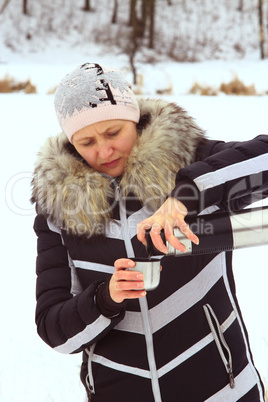 woman pouring hot tea from thermos bottle in the winter