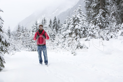 Young man with snow glasses hiking in wintry forest landscape