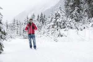Young man with snow glasses hiking in wintry forest landscape