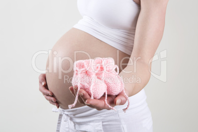 Pregnant woman holding pink baby shoes in her hands