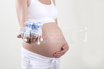 Pregnant woman holding blue baby shoes in her hands