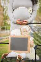 Pregnant Mom Behind Baby Girl in Chair Holding Blank Blackboard
