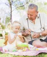 Grandfather and Granddaughter Coloring Easter Eggs on Blanket At