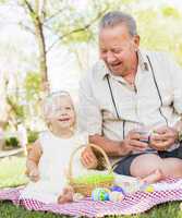 Grandfather and Granddaughter Coloring Easter Eggs on Blanket At