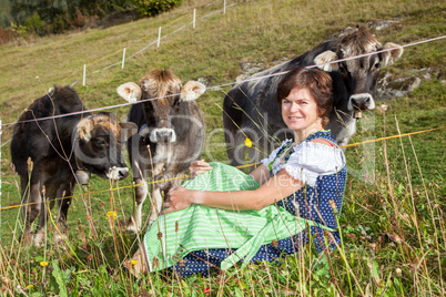 Woman in dirndl sitting in front of their cows