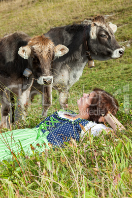 Woman in dirndl is before their cows in the grass