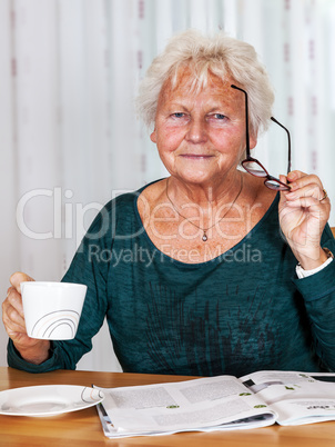 Elderly woman with cup looks up from reading