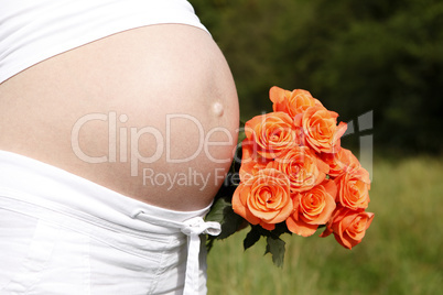 Pregnant woman outdoor with orange tulips in her hands