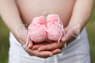 Pregnant woman outdoor with pink baby shoes in her hands