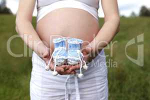 Pregnant woman outdoor with blue baby shoes in her hands