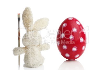 Stuffed Easter bunny paints a red Easter egg