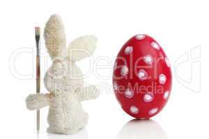 Stuffed Easter bunny paints a red Easter egg