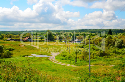 Rural landscape with dirt road, houses and power poles in the sp