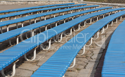 Row of blue wooden seats on a spectator grandstand photo. Bench in the park for the show