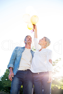 Cute couple holding up balloons at the park