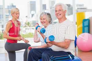 happy senior couple lifting dumbbells while instructor guiding t