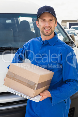 Delivery driver smiling at camera by his van holding parcel