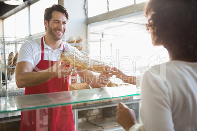 Smiling baker doing loaf transaction with customer